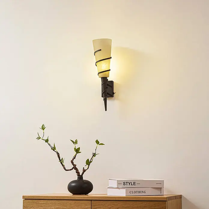 Lindby Wandleuchte Anouk - L x B x H: 16 x 12 x 44 cm, braun / rost, E14 - Wandleuchte mit beigem Milchglasschirm und dunklem, spiralförmigem Metallgestell, über Holzschrank beleuchtet.