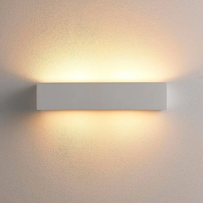 Lindby Wandleuchte Tjada - weiß / opal, G9 - Weiße, rechteckige Wandleuchte, die warmes Licht nach oben und unten auf eine strukturierte Wand wirft.