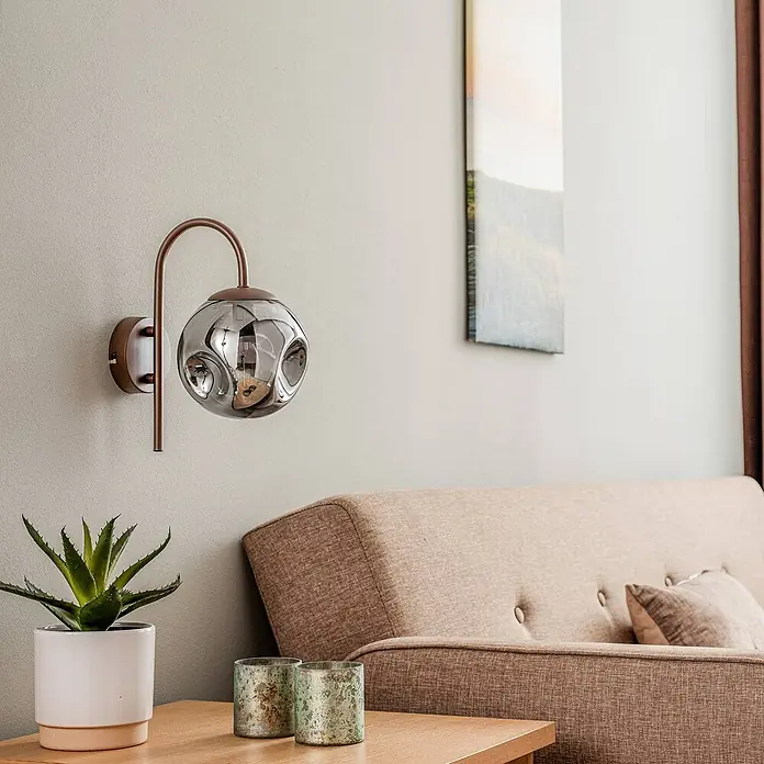Lindby Wandleuchte Valentina - braun / rost, alu / grau / zink, E14 - Bronzefarbene Wandleuchte mit Rauchglas-Kugel, beleuchtet einen modernen Wohnbereich.