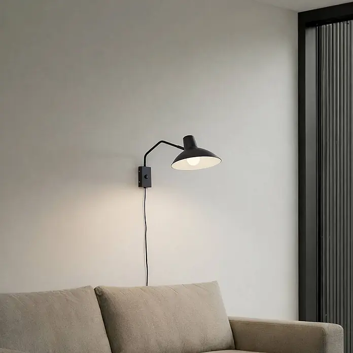 Lindby Wandleuchte Adrik - L x B x H: 48 x 23,5 x 23 cm, schwarz, schwarz, E27 - Schwarze verstellbare Wandleuchte mit sichtbarem Kabel, die ein helles Sofa beleuchtet.