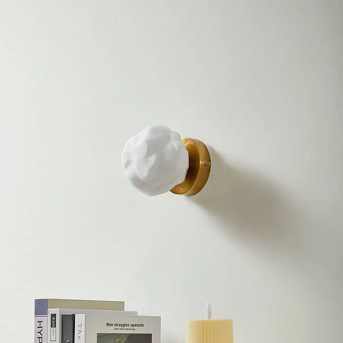 Lindby Wandleuchte Piatra - messing / gold, weiß / opal, G9 - Weiße Wolkenglas-Wandleuchte mit Messingfuß, über Büchern montiert.