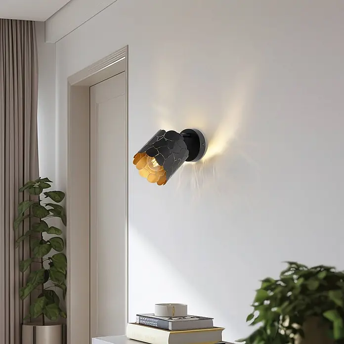 Lindby Wandleuchte Aralena - L x B x H: 12 x 12 x 12 cm, schwarz, schwarz, E27 - Schwarz-goldene Wandleuchte mit Muster, die eine weiße Wand in einem modernen Raum beleuchtet.