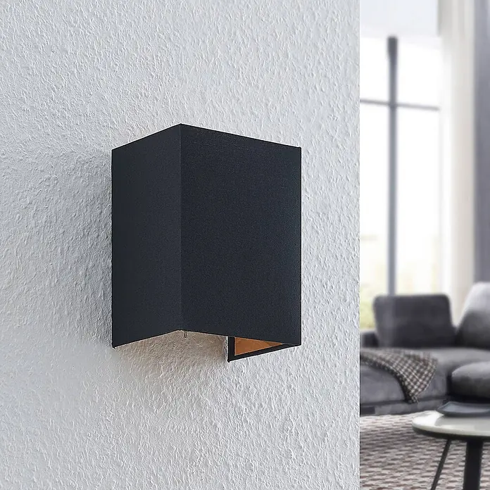 Lindby Wandleuchte Lukani - L x B x H: 12 x 15 x 20 cm, schwarz, E27 - Schwarze rechteckige Wandleuchte mit warmer goldener Innenseite, an texturierter weißer Wand.