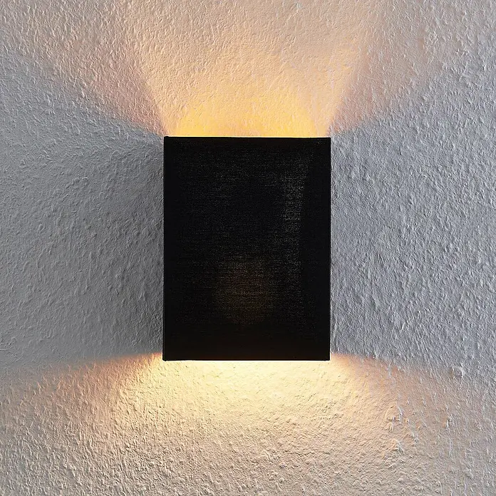 Lindby Wandleuchte Lukani - L x B x H: 12 x 15 x 20 cm, schwarz, E27 - Schwarze rechteckige Stoff-Wandleuchte, die warmes Licht nach oben und unten auf eine texturierte Wand wirft.