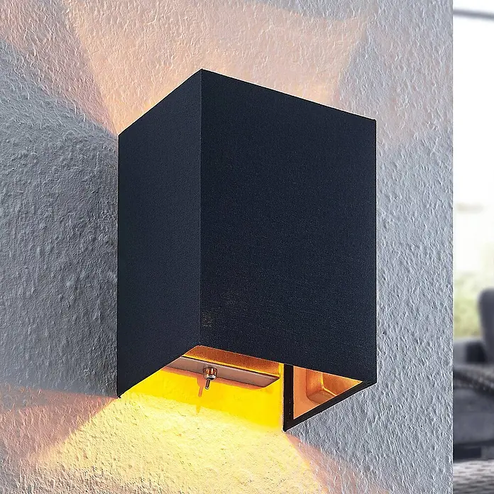 Lindby Wandleuchte Lukani - L x B x H: 12 x 15 x 20 cm, schwarz, E27 - Schwarze, rechteckige Wandleuchte wirft warmes gelbes Licht nach oben und unten an eine strukturierte Wand.