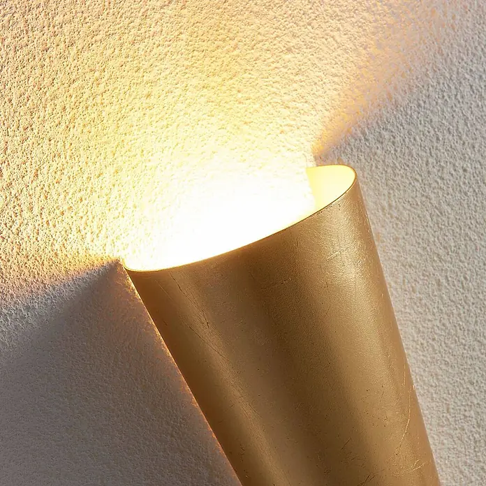 Lindby Wandleuchte Conan - messing / gold, messing / gold, G9 - Goldene halb-zylindrische Wandleuchte an einer texturierten Wand, die warmes Licht nach oben und unten wirft.