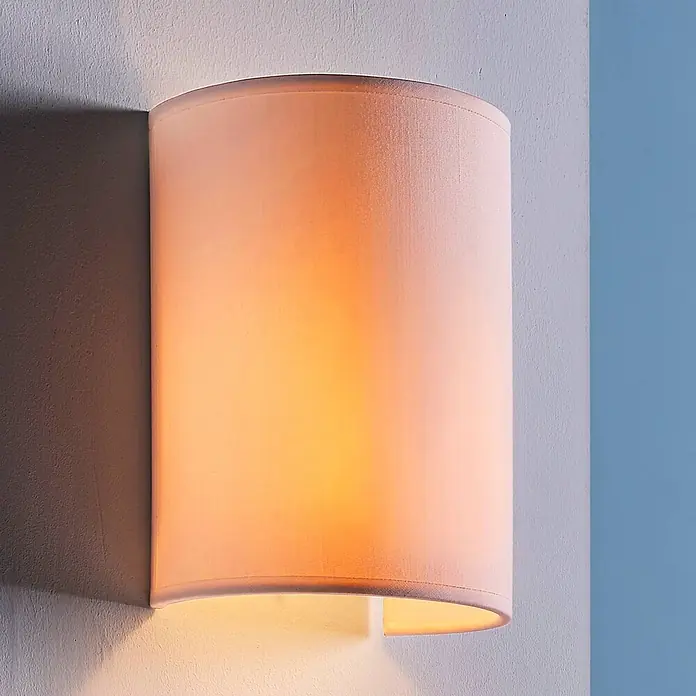 Lindby Wandleuchte Annalisa - weiß / opal, E27 - Beleuchtete Wandleuchte mit Stoffschirm, die warmes Licht nach oben und unten an einer hellen und blauen Wand abstrahlt.