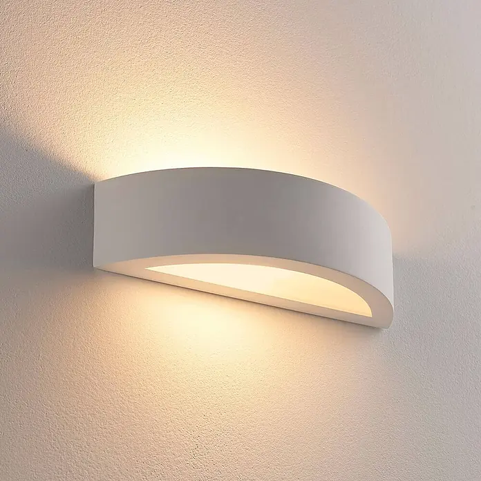 Lindby Wandleuchte Aurel - weiß / opal, E14 - Weiße, gebogene Wandleuchte, die warmes, indirektes Licht nach oben und unten auf eine strukturierte Wand wirft.