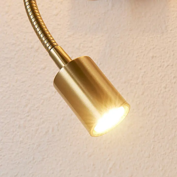 Lindby Wandleuchte Florens - messing / gold, E14 - Messing-LED-Lampe mit flexiblem Arm strahlt warmes Licht auf eine strukturierte Wand.