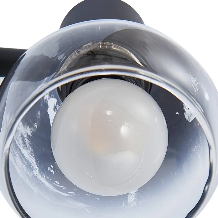 Lindby Wandleuchte Pendura - L x B x H: 9 x 9 x 12,5 cm, schwarz, alu / grau / zink, E14 - Klares Glasschirm einer Lampe mit einer weißen kugelförmigen Glühbirne und dunkler Halterung.
