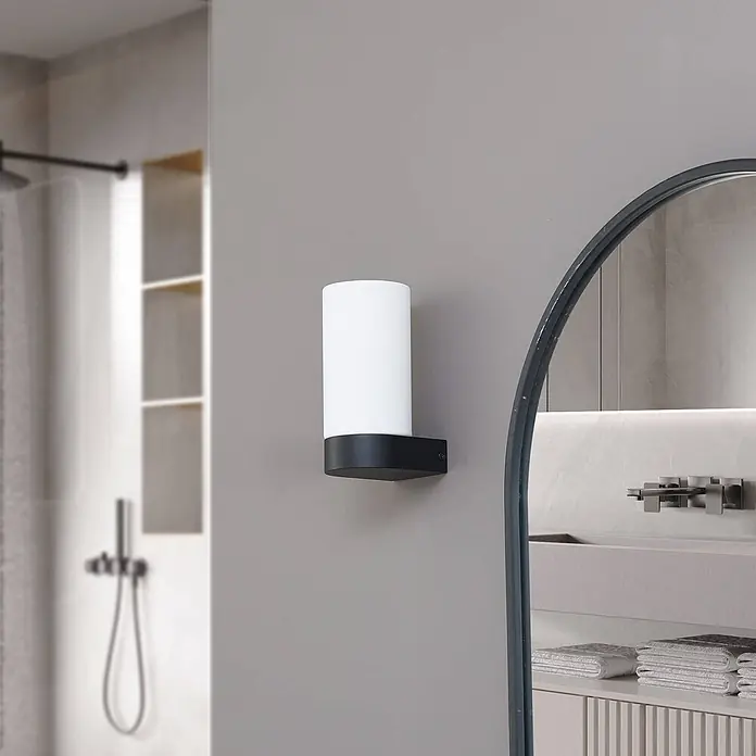 Lucande Wandleuchte Basolo - weiß / opal, E14 - Weiße zylindrische Wandleuchte mit schwarzem rechteckigem Sockel, in modernem Badezimmer montiert.