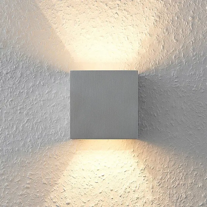 Arcchio Wandleuchte Zuzana - alu / grau / zink, G9 - Quadratische silberne Wandleuchte wirft warmes Licht nach oben und unten auf eine strukturierte Wand.