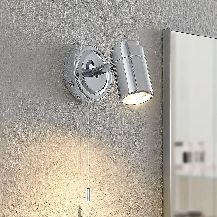 Lindby Wandleuchte Remilan - L x B x H: 12,3 x 9 x 10,6 cm, chrom / silber, chrom / silber, GU10 - Verstellbarer Chrom-Wandstrahler mit Zugschalter, beleuchtet eine strukturierte Wand neben einem Spiegel.