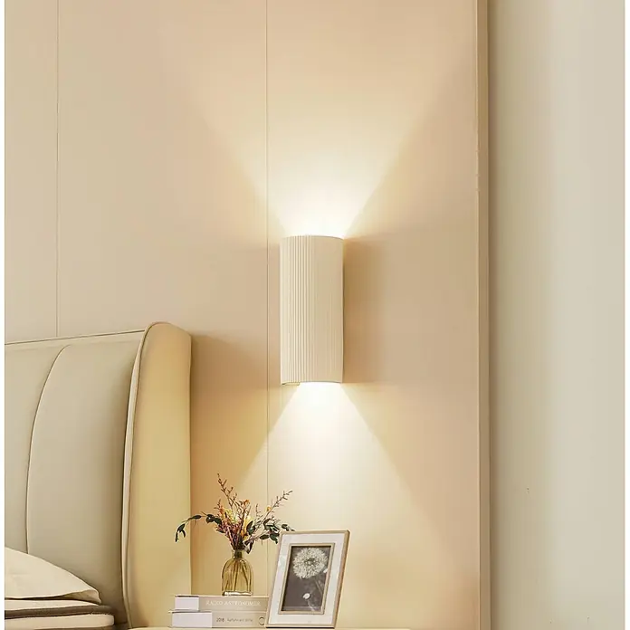Lindby Wandleuchte Colja - L x B x H: 9,6 x 13,3 x 30,5 cm, creme / amber, creme / amber, GU10 - Gerippte, cremefarbene Wandleuchte, die warmes Licht nach oben und unten abgibt, über einem Nachttisch im Schlafzimmer montiert.