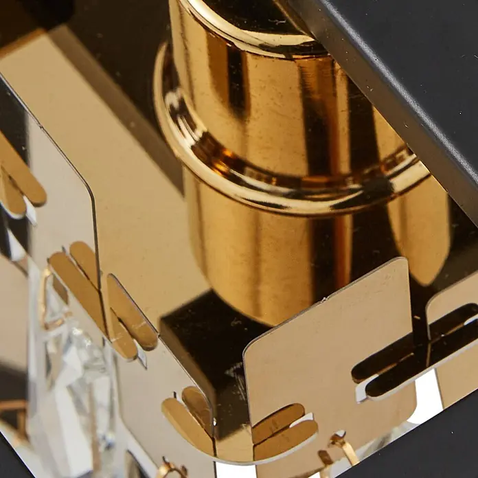 Lucande Wandleuchte Arcan - L x B x H: 20,4 x 15 x 20,4 cm, schwarz, E14 - Nahaufnahme einer goldfarbenen Metallleuchte mit schwarzem Rahmen und klaren facettierten Kristallelementen.