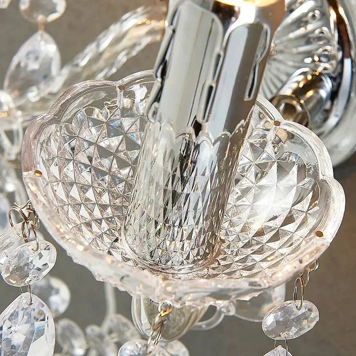 Lindby Wandleuchte Merida - L x B x H: 18,5 x 33 x 35 cm, chrom / silber, klar / transparent, E14 - Nahaufnahme einer klaren, facettierten Kristall-Leuchtenfassung mit Chrombeschlag und hängenden Kristalldekorationen.