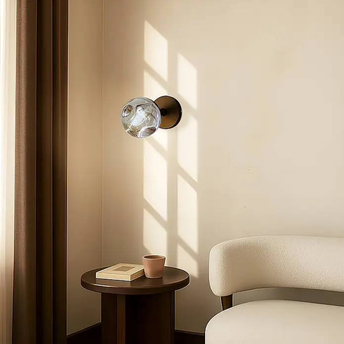 Lindby Wandleuchte Valentina - schwarz, alu / grau / zink, G9 - Moderne Wandleuchte mit gemusterter Glaskugel und dunklem Metallsockel, an cremefarbener Wand in einem Wohnraum montiert.