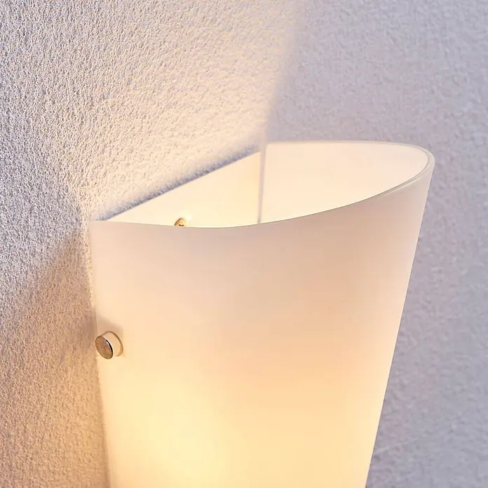 Lindby Wandleuchte Aurora - L x B x H: 11 x 12 x 28 cm, weiß / opal, E27 - Wandleuchte aus mattiertem Glas auf einer strukturierten Wand, die ein warmes Licht abgibt.