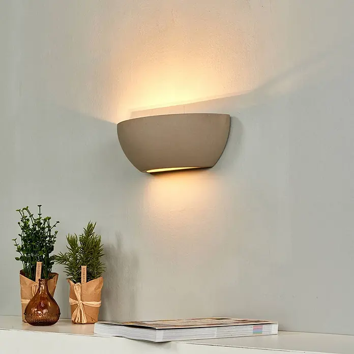 Lindby Wandleuchte Renata - alu / grau / zink, E14 - Graue Beton-Wandleuchte in Schalenform, die warmes Licht nach oben und unten an eine strukturierte Wand strahlt.