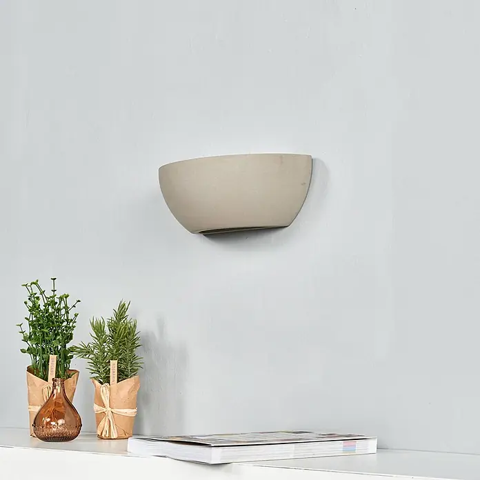 Lindby Wandleuchte Renata - alu / grau / zink, E14 - Beige halbrunde Wandleuchte über einem Regal mit Zierpflanzen.