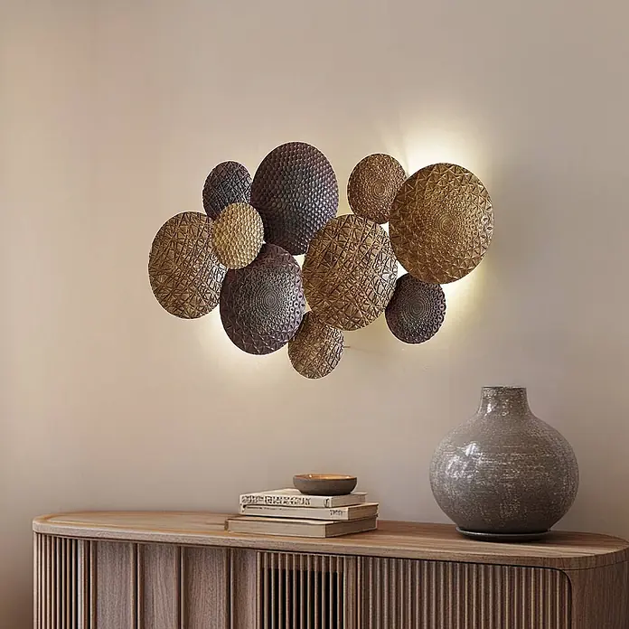Lindby Wandleuchte Soraya - messing / gold, E27 - Texturierte, metallische Wandkunst aus Kreisen mit integrierter Hintergrundbeleuchtung, über einer Holzkonsole angebracht.