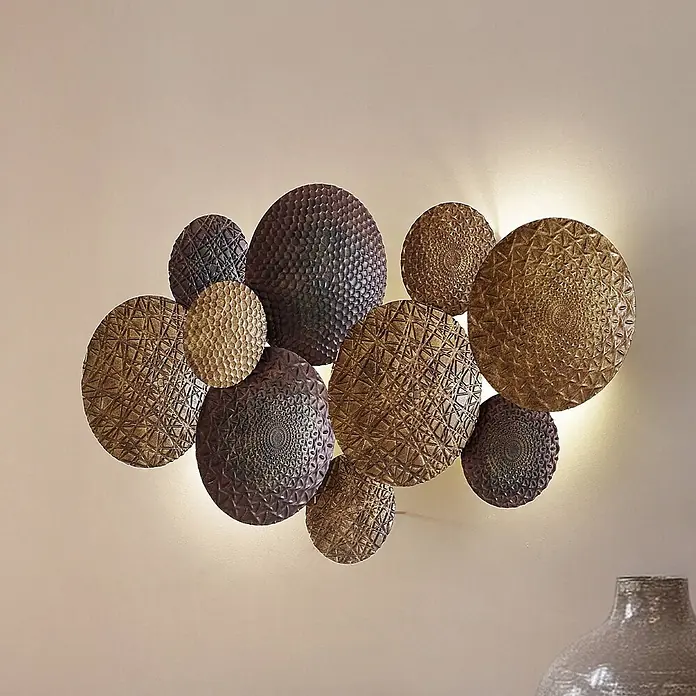 Lindby Wandleuchte Soraya - messing / gold, E27 - Strukturierte Wanddekoration aus runden Metallplatten in Bronze und Dunkelbraun mit Hintergrundbeleuchtung, die ein warmes Leuchten erzeugt.