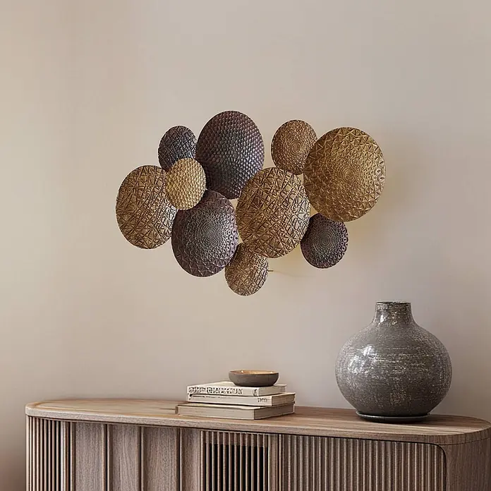 Lindby Wandleuchte Soraya - messing / gold, E27 - Texturierte gold- und bronzefarbene runde Metall-Wanddekoration, kunstvoll über einem Holzschrank arrangiert.
