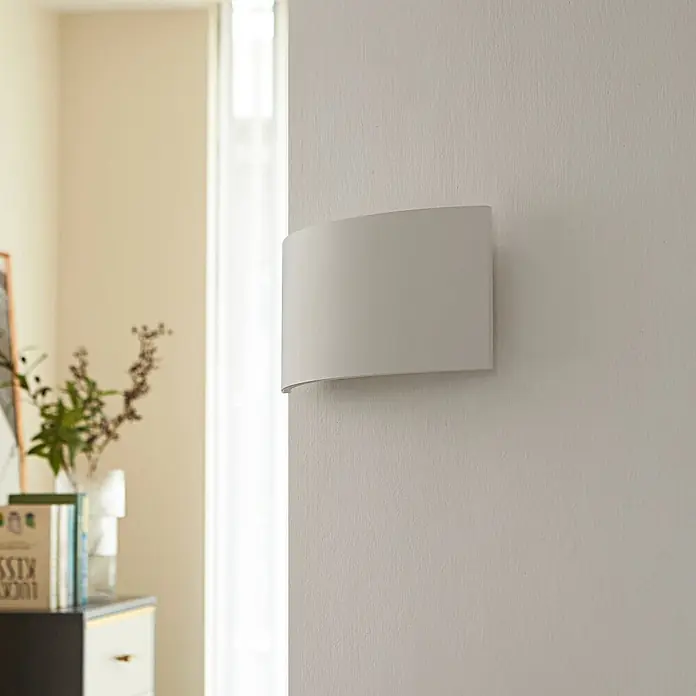 Lindby Wandleuchte Naike - L x B x H: 8 x 35 x 15 cm, weiß / opal, weiß / opal, G9 - Weiße, gebogene Wandleuchte, die indirektes Licht spendet, an einer hellen Wand montiert.