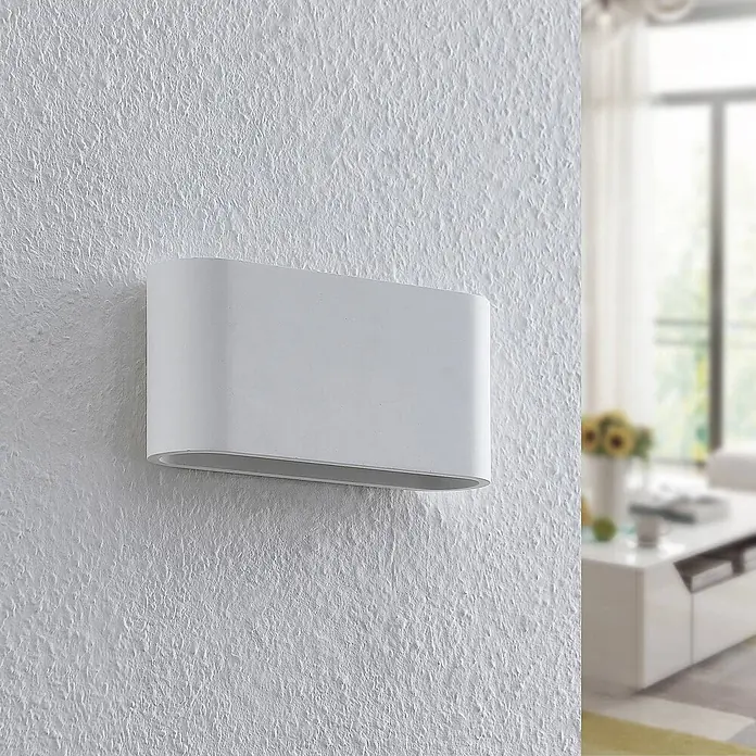 Lindby Wandleuchte Mavora - L x B x H: 7 x 25 x 12 cm, weiß / opal, G9 - Weiße ovale Wandleuchte an einer strukturierten Wand, die ihre Anwendung in einem unscharfen Raum zeigt.