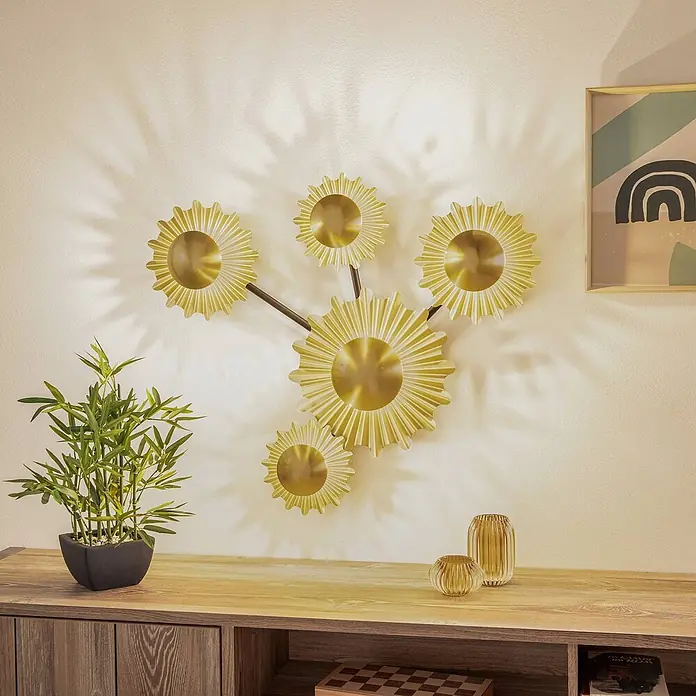 Lindby Wandleuchte Senmia - messing / gold, G9 - Goldene metallische Wanddekoration mit mehreren sonnenförmigen Elementen über einem Holzkonsolentisch.