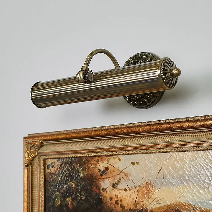 Lindby Wandleuchte Joely - bronze / altmessing, bronze / altmessing, E14 - Antike Messing-Bilderleuchte mit geripptem Schirm, über einem gerahmten Gemälde montiert.