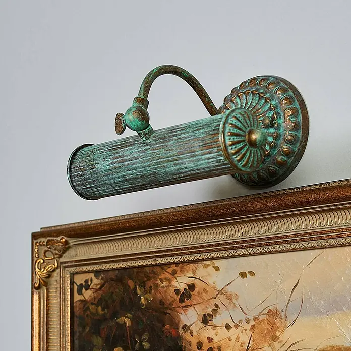 Lindby Wandleuchte Beno - bronze / altmessing, bronze / altmessing, E14 - Verzierte Bilderleuchte mit kupferfarbener Patina beleuchtet ein gerahmtes Kunstwerk.