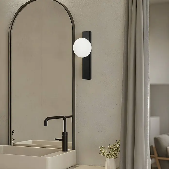 Lindby Wandleuchte Tavrik - schwarz, weiß / opal, G9 - Schwarze Wandleuchte mit weißem kugelförmigem Diffusor, neben einem Bogenspiegel über einem Waschbecken montiert.