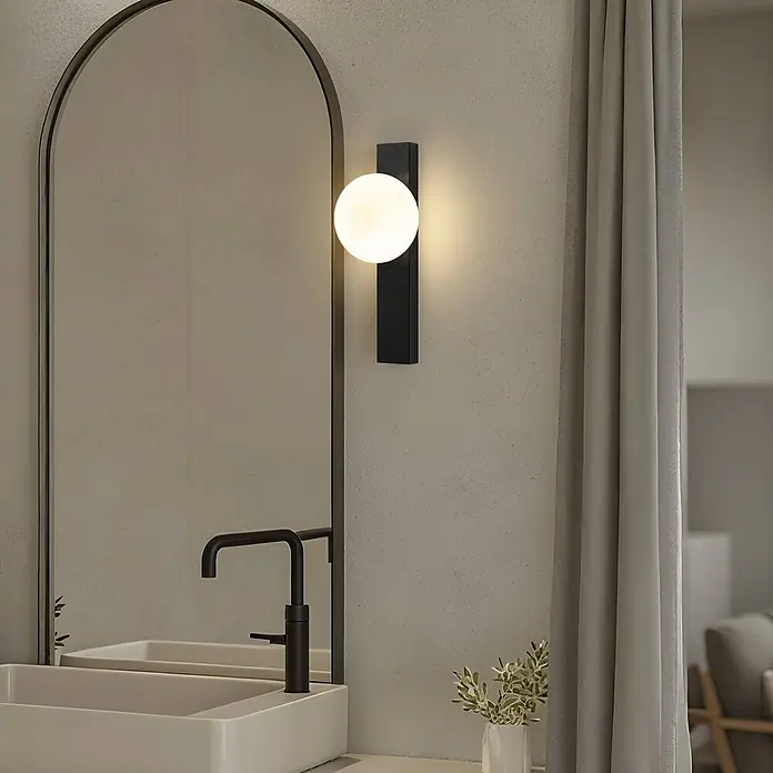 Lindby Wandleuchte Tavrik - schwarz, weiß / opal, G9 - Moderne schwarze Wandleuchte mit kugelförmigem weißem Diffusor, die einen Badezimmerwaschtisch beleuchtet.
