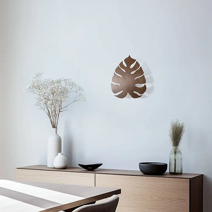 Envostar Wandleuchte Folah - Holz dunkel, Holz dunkel, G9 - Kupferfarbene Monstera-Blatt-Wanddekoration, an einer Wand über einem Holzschrank montiert.