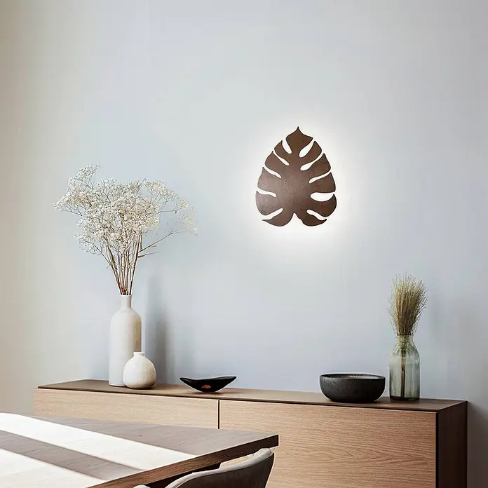 Envostar Wandleuchte Folah - Holz dunkel, Holz dunkel, G9 - Dunkle, Monstera-blattförmige Wandleuchte mit indirekter warmer Beleuchtung, über einem Holzbuffet montiert.