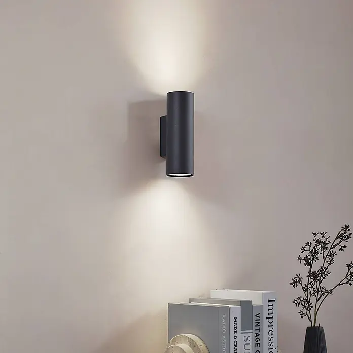 Lindby Wandleuchte Joffrey - schwarz, schwarz, GU10 - Dunkelgraue zylindrische Wandleuchte mit Up- und Downlight-Effekt an einer hellen Wand.