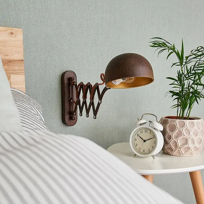 Lindby Wandleuchte Curtis - L x B x H: 57 x 13 x 23 cm, braun / rost, braun / rost, E14 - Rustikale, dunkelbraune Wandlampe mit Scherengelenk und goldener Schirminnenseite, neben einem Bett.