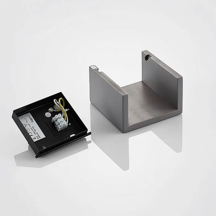 Lindby Wandleuchte Smira - L x B x H: 7,5 x 12,5 x 12,5 cm, alu / grau / zink, G9 - Schwarze Elektrobasis mit Verkabelung und grauem U-förmigem Metall-Leuchtengehäuse.