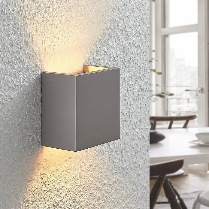 Lindby Wandleuchte Smira - L x B x H: 7,5 x 12,5 x 12,5 cm, alu / grau / zink, G9 - Graue rechteckige Wandlampe beleuchtet eine strukturierte Wand in einem modernen Esszimmer.