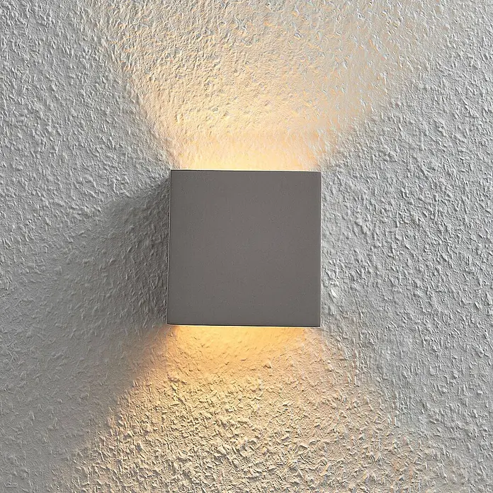 Lindby Wandleuchte Smira - L x B x H: 7,5 x 12,5 x 12,5 cm, alu / grau / zink, G9 - Graue quadratische Wandleuchte, die eine strukturierte Wand mit warmem Licht nach oben und unten beleuchtet.