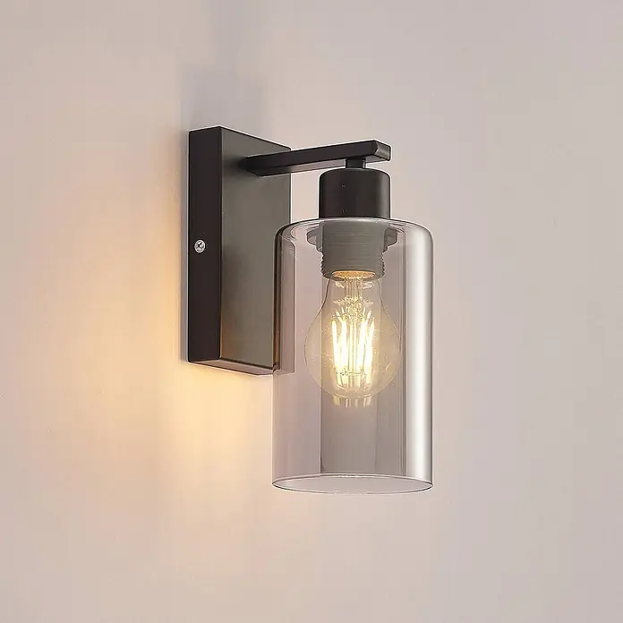 Lindby Wandleuchte Emavi - L x B x H: 15 x 10 x 23 cm, schwarz, schwarz, E27 - Moderne schwarze Wandleuchte aus Metall mit zylindrischem Klarglasschirm und sichtbarer Vintage-LED-Birne, die warmes Licht abstrahlt.