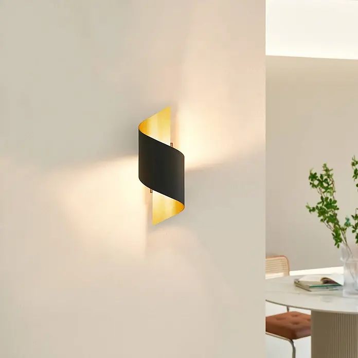 Lindby Wandleuchte Desirio - L x B x H: 10,5 x 8 x 24 cm, schwarz, G9 - Schwarze und goldene S-förmige Wandleuchte, die nach oben und unten leuchtet, an einer Wand im Raum.