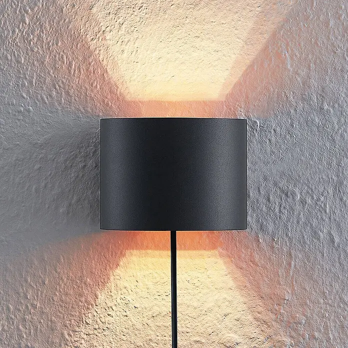 Arcchio Wandleuchte Zuzana - L x B x H: 11,2 x 13 x 9,7 cm, schwarz, G9 - Matte schwarze zylindrische Wandleuchte, die warmes Licht nach oben und unten auf eine strukturierte Wand wirft.