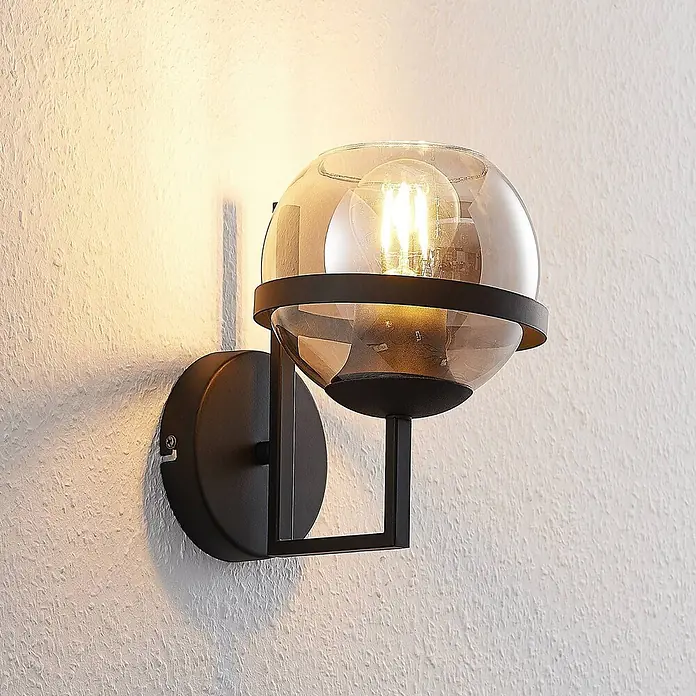 Lindby Wandleuchte Marinka - schwarz, klar / transparent, E27 - Wandleuchte aus schwarzem Metall mit rauchfarbenem Glaskugel und beleuchteter Glühbirne.