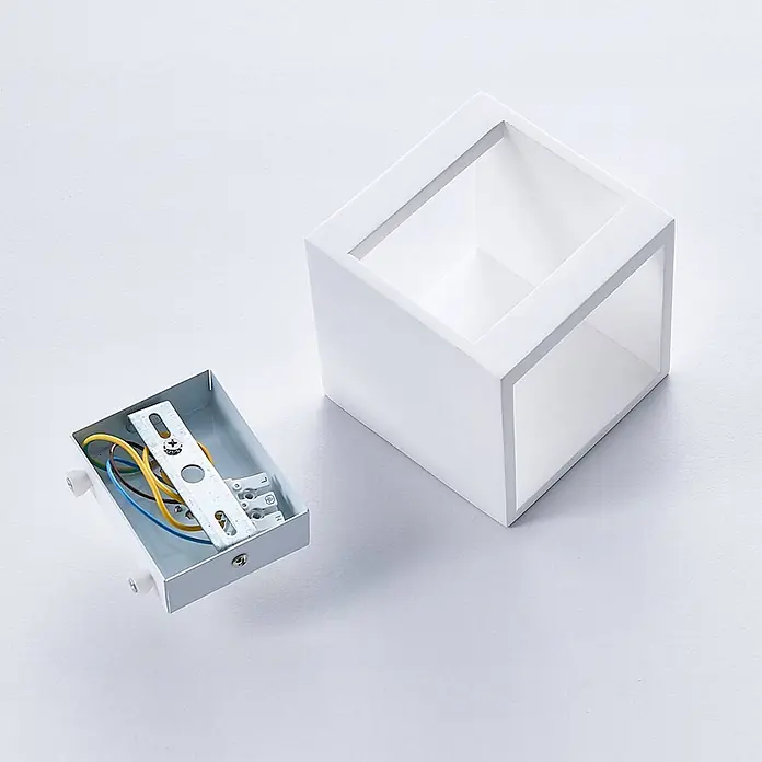 Lindby Wandleuchte Kay - L x B x H: 11,5 x 11,5 x 11,5 cm, weiß / opal, G9 - Weißes rechteckiges Wandleuchtengehäuse neben seiner internen Metallhalterung mit farbigen Kabeln.