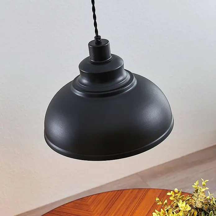 Lindby Pendelleuchte Albertine - L x B x H: 29 x 29 x 19,7 cm, schwarz, Schwarz, gold, E27 - Mattschwarze Industrie-Pendelleuchte aus Metall über einem Holztisch.