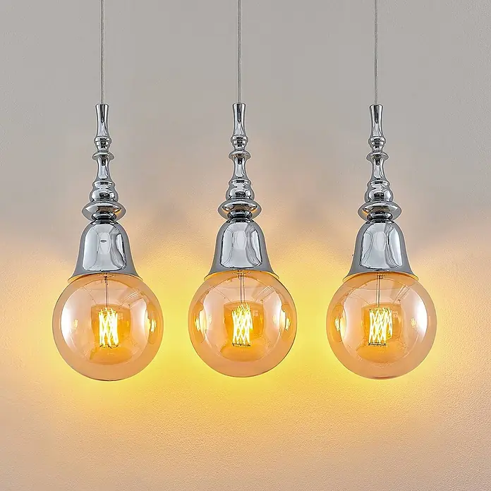 Lucande Pendelleuchte Gesja - L x B x H: 63,5 x 13,5 x 32,5 cm, chrom, E27 - Drei verschnörkelte Chrom-Pendelleuchten mit bernsteinfarbenen Glaskugelschalen und warmen LED-Filamentbirnen.
