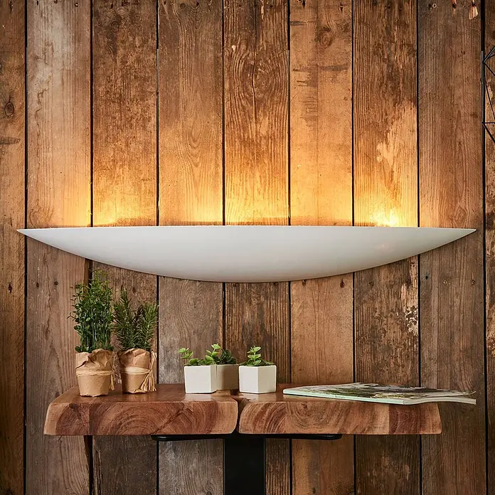 Lindby Wandleuchte Tommi - weiß / opal, E14 - Elegante weiße, gekrümmte Wandleuchte, die eine rustikale Holzwand nach oben beleuchtet.