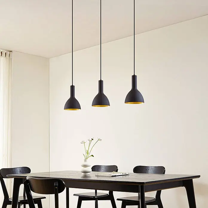 Arcchio Pendelleuchte Cosmina - L x B x H: 100 x 17,5 x 26 cm, schwarz, Schwarz, gold, E27 - Drei schwarze Pendelleuchten mit goldenen Innenseiten hängen über einem dunklen Esstisch aus Holz, der mit Stühlen und einer Blumenvase gedeckt ist.